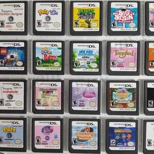 May include: A collection of 18 Nintendo DS game cartridges, displayed in a clear plastic case. The cartridges feature a variety of popular games, including "Imagine: Fashion Designer", "Petz Catz Clan", "Plants vs. Zombies", "Big Brain Academy", "Dora Saves the Mermaids", "Lego Harry Potter", "Dora & Puppy", "Ice Age: Dawn of the Dinosaurs", "Tangled", "Tinkerbell and the Lost Treasure", "Imagine: Zookeeper", "Hello Kitty Party", "Disney Princess", "Gardening Mama", "Catz", "My Little Pony", "Cooking Mama", "Team Umizoomi", and "Imagine: Bobyz".