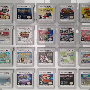 Puede incluir: Una colección de 16 cartuchos de juego de Nintendo 3DS que se muestran en una caja de plástico transparente. Los cartuchos están dispuestos en cuatro filas de cuatro. Los cartuchos son de diferentes colores y tienen diferentes títulos de juegos.