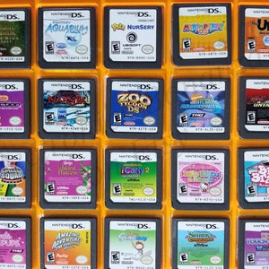 Könnte beinhalten: Eine Sammlung von 20 Nintendo DS-Spielkassetten in einem durchsichtigen Plastik-Etui. Die Kassetten sind in vier Reihen zu je fünf angeordnet. Die Kassetten sind alle in verschiedenen Farben und haben unterschiedliche Titel. Einige der Titel sind "Fluch der Karibik: Der Fluch des schwarzen Perls", "Fantasy Aquarium", "Pets Nursery", "Mario Party DS", "The Urbz", "Puzzle Collection Zoo", "Narnia", "Zoo Tycoon DS", "Atlantis Squarepantis", "Untamed", "Marvel Super Hero Squad", "Barbie Island Princess", "iCarly 2", "Hello Kitty and Friends", "Big Brain Academy", "Barbie: Die Prinzessin und die Bettlerin", "Amazing Adventures: The Forgotten King", "Scribblenauts", "Shrek's Carnival Countdown" und "101 Touch Games".