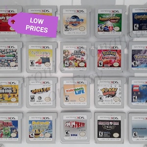 Può includere: Una collezione di 16 cartucce di gioco per Nintendo 3DS esposte in una custodia di plastica trasparente. Le cartucce sono disposte in quattro file di quattro. Le cartucce sono tutte di colori diversi e hanno titoli di gioco diversi. Il testo "LOW PRICES" è scritto su un'etichetta viola nell'angolo in alto a sinistra dell'immagine.