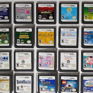 May include: A collection of Nintendo DS game cartridges, each with colorful game art and titles. Games include "Hot Wheels," "Tinkerbell," "Brain Age," "Rock Band," and "Lego Harry Potter." The cartridges are arranged in a grid.