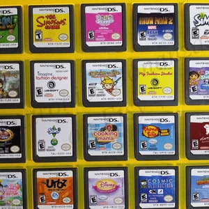 May include: A collection of 18 Nintendo DS game cartridges, displayed in a yellow plastic case. The cartridges feature a variety of popular games, including Scooby-Doo, The Simpsons, Iron Man 2, The Sims 2, Lego Lord of the Rings, Imagine Fashion Designer, Down the Life, My Fashion Studio, Pet Shelter, Cooking Mama, Phineas and Ferb, Nintendogs, Dora the Explorer, The Urbz, Disney Princess, Cosmic Destruction, and Super Slam.