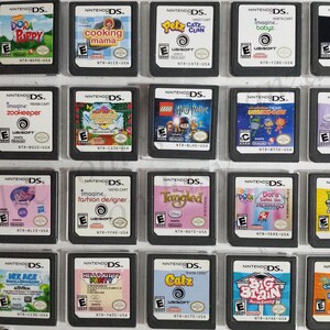 May include: A collection of 18 Nintendo DS game cartridges, organized in a clear plastic case. The cartridges feature a variety of popular children's characters and themes, including Dora the Explorer, Hello Kitty, Disney Princesses, and more.