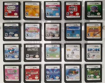 Może przedstawiać: Kolekcja 20 gier na Nintendo DS w czarnych pudełkach. Gry są ułożone w cztery rzędy po pięć. Gry obejmują tytuły takie jak "Wizards", "Brain Age", "Cooking Mama 3", "Call of Duty 4", "Shrek", "Spore Creatures", "Sally's Salon", "Brain Age 2", "Super Mario" i "Tinker Bell".