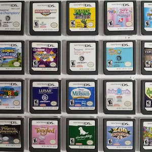 May include: A collection of 20 Nintendo DS game cartridges displayed in a clear plastic case. The cartridges are arranged in four rows of five, with each cartridge featuring a different game title and cover art. Some of the games include "Plants vs. Zombies", "Sonic Sega All-Stars Racing", "Super Mario", "Tangled", and "Zoo Hospital".