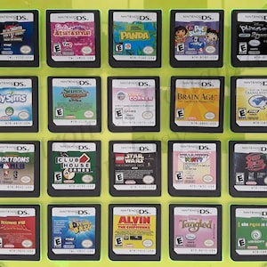 Puede incluir: Una colección de 18 cartuchos de juego de Nintendo DS que se muestran en una caja de plástico verde. Los cartuchos están dispuestos en tres filas de seis. Los cartuchos son de diferentes colores y tienen diferentes títulos, incluyendo "My Sims", "Brain Age", "Nicktoons MLB", "LEGO Star Wars", "Kung Fu Panda" y "Tangled".