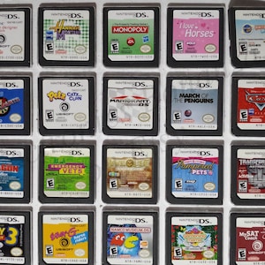Puede incluir: Una colección de 16 cartuchos de juego de Nintendo DS, dispuestos en un patrón de cuadrícula. Los cartuchos están dispuestos en cuatro filas de cuatro, con cada cartucho presentando un título de juego y una portada de arte diferentes. Algunos de los juegos incluyen "Hannah Montana", "Monopoly", "Me encantan los caballos", "Dragon", "Veterinarios de emergencia", "Jewel Quest", "Mascotas mimadas", "Transformers Autobots", "Toy Story 3", "Mi entrenador Sat", y "Cars".
