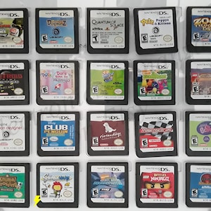 May include: A collection of 20 Nintendo DS game cartridges displayed in a clear plastic case. The cartridges are arranged in four rows of five. The cartridges are all different colors and have different game titles on them. Some of the titles include "Animal Crossing", "Club Penguin", "Dora the Explorer", "Metroid Hunters", and "Zoo Tycoon 2".