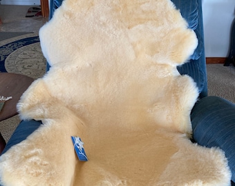 May include: A cream-colored sheepskin rug is draped over a blue armchair. The rug has a natural, fluffy texture and is a soft, warm addition to any home.