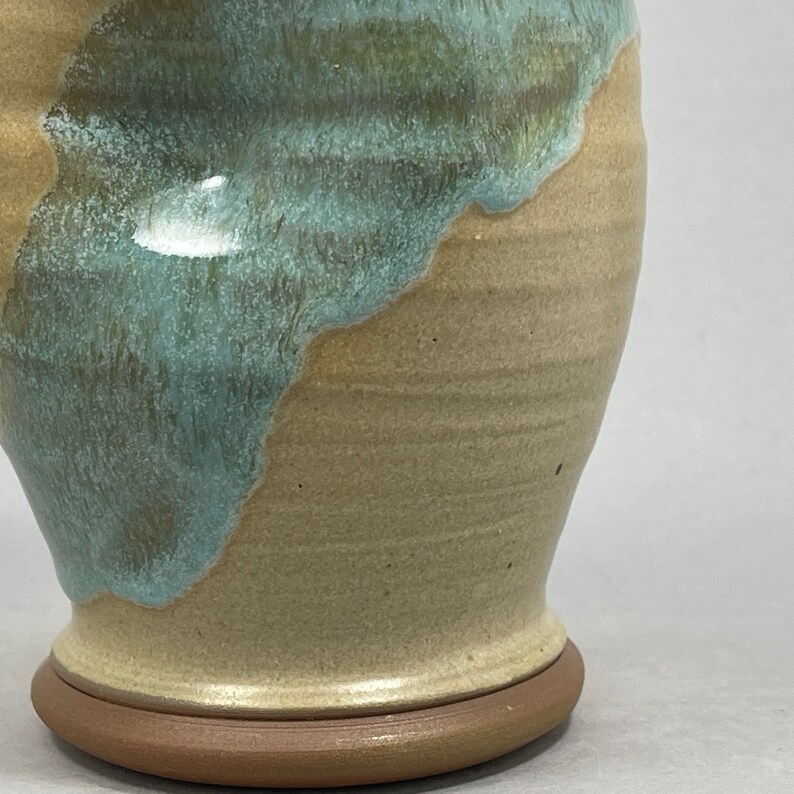 May include: A ceramic vase with a light brown glaze and a blue-green glaze on the top half. The vase has a rounded body and a wide base.