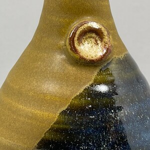 May include: A ceramic vase with a brown and blue glaze. The vase has a round, raised knob on the side.