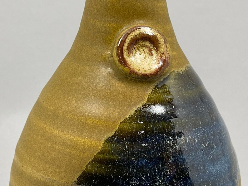 May include: A ceramic vase with a brown and blue glaze. The vase has a round, raised knob on the side.
