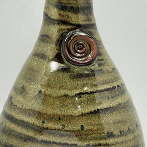 May include: A handcrafted ceramic vase with a unique, organic shape. The vase features a blend of olive green and dark brown horizontal stripes. A spiral design in shades of brown adorns the side, adding a decorative touch. The vase is a decorative item.
