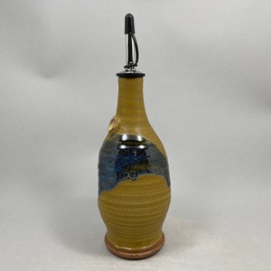 May include: A ceramic olive oil bottle with a brown and blue glaze. The bottle has a spout with a black and silver pourer.
