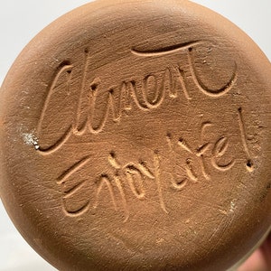 May include: Close-up of the bottom of a terracotta pot with the inscription "Clement Enjoy Life!" in cursive.