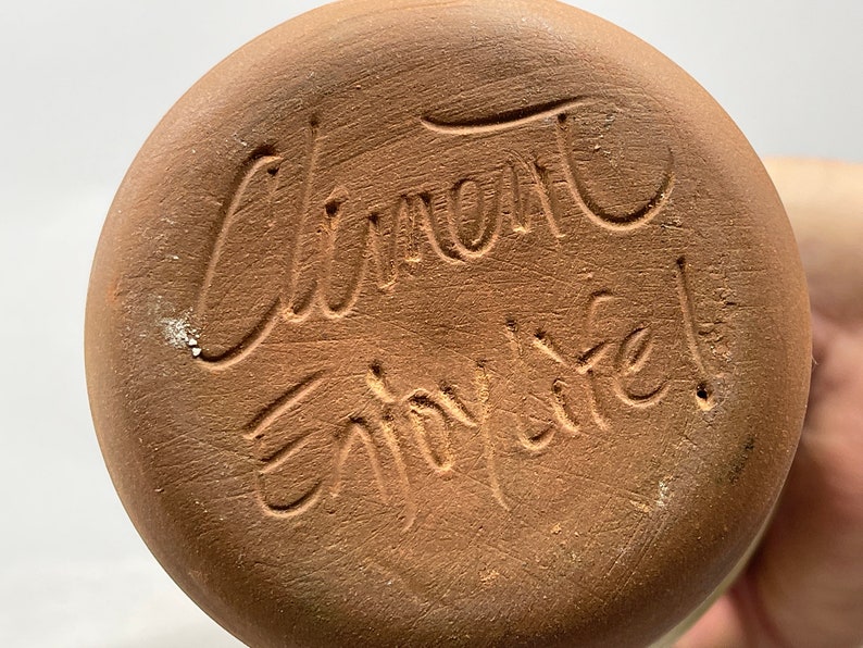 May include: Close-up of the bottom of a terracotta pot with the inscription "Clement Enjoy Life!" in cursive.