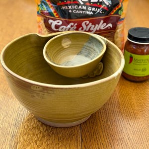 May include: A ceramic serving bowl set with a large bowl and a smaller, attached bowl. A jar of salsa and a bag of tortilla chips are in the background. The salsa jar has a green label with the word "Mild" on it.