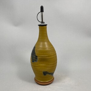 May include: A yellow ceramic oil and vinegar bottle with a black and blue glaze. The bottle has a stainless steel pour spout with a black rubber stopper.