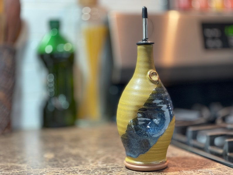 May include: A handmade ceramic olive oil bottle with a yellow and blue glaze. The bottle has a spout with a metal pourer.