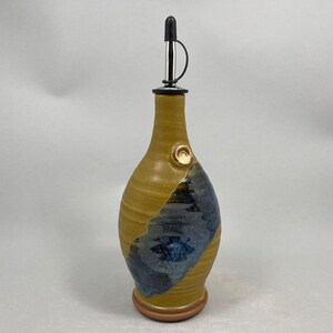 May include: A handmade ceramic olive oil bottle with a blue and yellow glaze. The bottle has a spout with a black stopper and a small knob on the side.