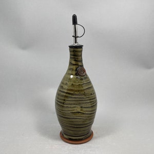 May include: A handcrafted ceramic olive oil bottle with a dark green and brown striped pattern. It features a stainless steel spout with a black cap and a decorative spiral accent. The bottle stands approximately 10 inches tall.