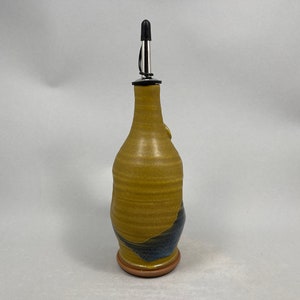 May include: A ceramic olive oil bottle with a yellow and blue glaze. The bottle has a stainless steel pour spout with a black rubber stopper.