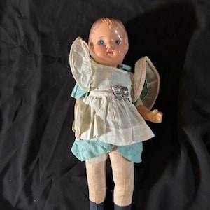 May include: A vintage doll with a painted porcelain face, blue eyes, and a white dress with blue accents. The doll has a fabric body and is wearing black shoes.