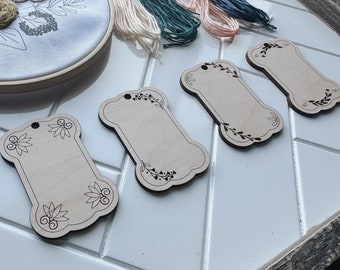 May include: Four unfinished wooden tags featuring a floral design and a blank space for writing. The tags are ideal for adding a personal touch to gifts or crafts.