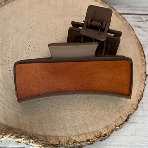 May include: A brown plastic hair clip with a wood-like texture on the top. The clip has a spring mechanism to hold hair in place.