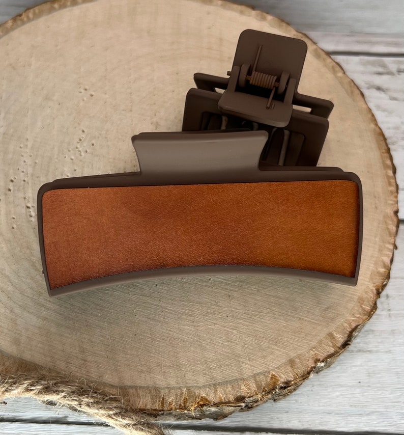 May include: A brown plastic hair clip with a wood-like texture on the top. The clip has a spring mechanism to hold hair in place.