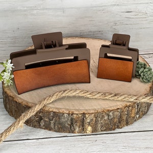 May include: Two brown plastic hair clips with a brown leather-like insert. The larger clip is curved and the smaller clip is rectangular.