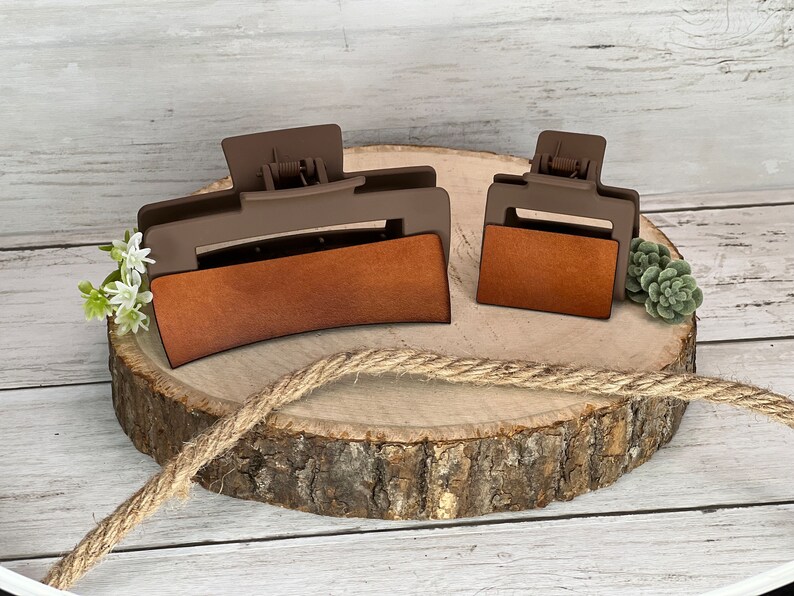 May include: Two brown plastic hair clips with a brown leather-like insert. The larger clip is curved and the smaller clip is rectangular.