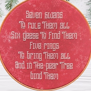 Può includere: Un cerchio da ricamo rosso con testo bianco che recita "Seven Swans To rule them all Six geese To find them Five rings To bring them all and in the pear tree bind them". Il cerchio ha un diametro di 20 cm ed è ricamato con un motivo a fiocco di neve. Il testo "Stitched Example [18ct Snowflake aida from EasyStitchForFun | 8" hoop]" è sotto il cerchio. Il testo "PDF Pattern" è nell'angolo in alto a destra dell'immagine.
