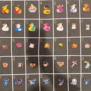 May include: A collection of 35 colorful rubber charms, including ducks, cartoon characters, and other whimsical designs. The charms are arranged in a grid on a dark background, showcasing a variety of shapes and colors.