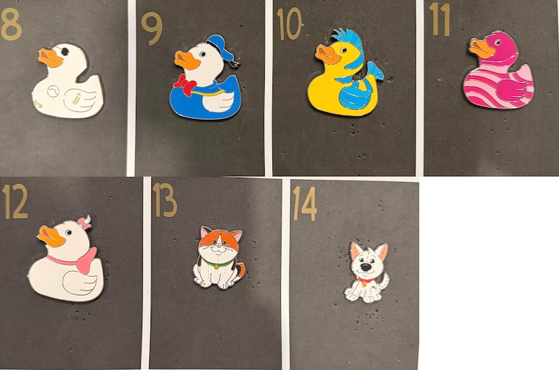 May include: A collection of colorful cartoon animal-shaped pins. The pins include a white duck, a duck wearing a blue sailor outfit, a yellow duck with blue hair, a pink duck with white stripes, a duck with a pink bow, a cat, and a dog.