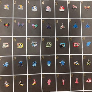 May include: A collection of 35 enamel pins, each with a unique design. The pins feature various cartoon characters, castles, and celebratory text. The pins are arranged on a black grid, showcasing a variety of colors and styles.