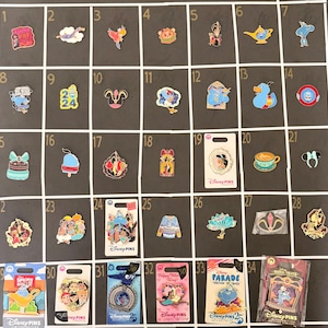 May include: A collection of thirty-four Disney character enamel pins arranged in a numbered grid. The pins feature various animated figures, objects, and icons, including Genie, Aladdin, Jasmine, and Jafar, displayed both loose and on branded backing cards.