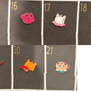 May include: A collection of colorful enamel pins featuring cartoon characters and objects. The pins include a red warthog, a pink frog, a white cat with a pink collar, a yellow and orange hat, and a green and brown hat.