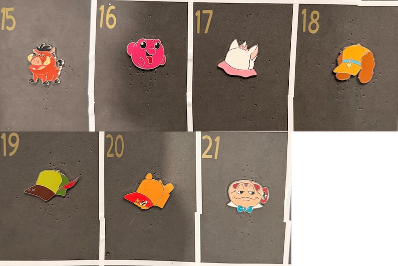 May include: A collection of colorful enamel pins featuring cartoon characters and objects. The pins include a red warthog, a pink frog, a white cat with a pink collar, a yellow and orange hat, and a green and brown hat.