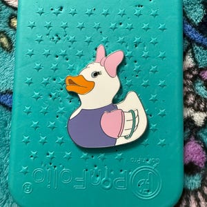 May include: A teal-colored case with a star pattern and a cartoon duck pin. The duck pin has a white body, orange beak, and wears a pink bow, purple top, and pink heart-shaped accessory. The case has the text "www.Gopinpro.com".