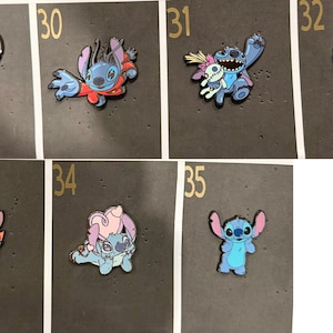 May include: A collection of enamel pins featuring the character Stitch from the animated film Lilo & Stitch. The pins depict Stitch in various poses, including playing a ukulele, surfing, and holding a voodoo doll. The pins are blue, pink, and red.