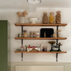 May include: A green metal locker cabinet with two doors and a set of three wooden shelves with various kitchen items, including jars of pasta, a white colander, and a vintage scale.