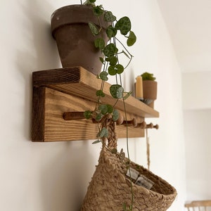 May include: A wooden shelf with hooks and a small plant in a terracotta pot. A woven basket hangs from one of the hooks.