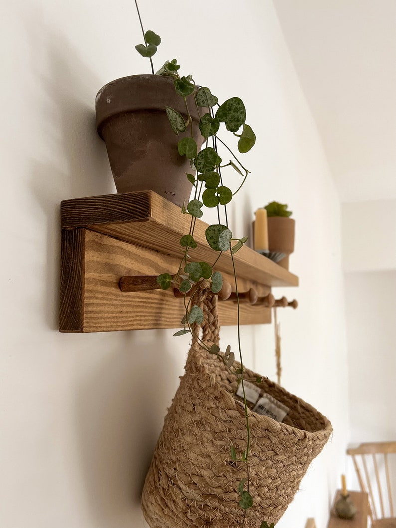 May include: A wooden shelf with hooks and a small plant in a terracotta pot. A woven basket hangs from one of the hooks.