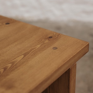Pode incluir: Uma superf&iacute;cie de mesa de madeira castanho-clara com um padr&atilde;o de gr&atilde;o de madeira vis&iacute;vel e um pequeno detalhe de tamp&atilde;o de madeira circular castanho-escuro embutido perto da borda do canto do tampo retangular da mesa.