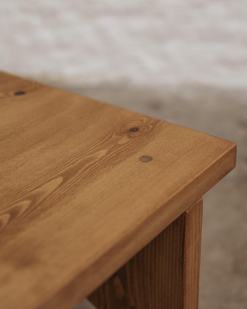 Pode incluir: Uma superf&iacute;cie de mesa de madeira castanho-clara com um padr&atilde;o de gr&atilde;o de madeira vis&iacute;vel e um pequeno detalhe de tamp&atilde;o de madeira circular castanho-escuro embutido perto da borda do canto do tampo retangular da mesa.