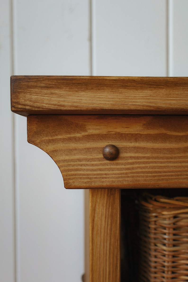 May include: Close-up of the top corner of a wooden cabinet with a brown stain. The cabinet has a decorative detail on the top edge and a small, round, brown knob.