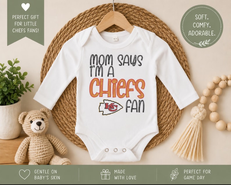May include: White baby bodysuit with long sleeves, featuring the text "MOM SAYS I'M A CHIEFS FAN" in black and orange. The Kansas City Chiefs logo is also displayed. The bodysuit is hanging on a wooden hanger.