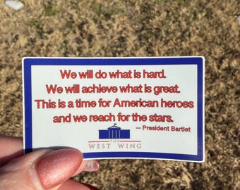 May include: A rectangular sticker with a white background and a dark blue border. It features red text that reads: We will do what is hard. We will achieve what is great. This is a time for American heroes and we reach for the stars. - President Bartlet. Below the text is a blue icon of the White House and the words THE WEST WING.