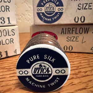 May include: A spool of brown thread with a white label that reads "Pure Silk OO Utica Threads OO Machine Twist".